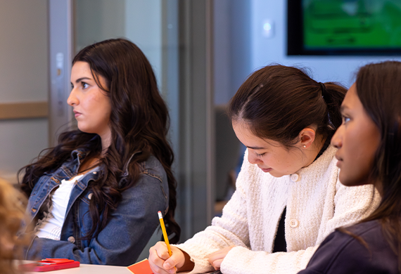 Image of three Marist University students taking notes and listening during class.