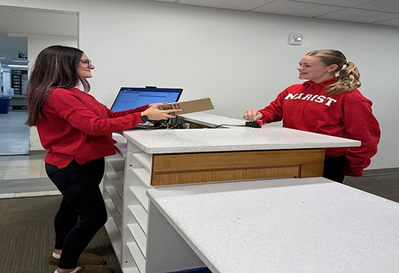 A photo with two Marist students in the Mail and Package Center, one is receiving a package from a student employee.