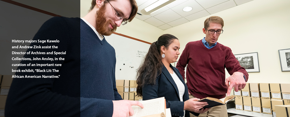 History majors Sage Kawelo and Andrew Zink assist the Director of Archives and Special Collections, John Ansley, in the curation of an important rare book exhibit, “Black Lit: The African American Narrative.