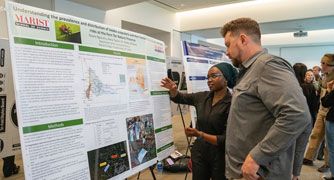 Image of a student presenting a research project to a faculty member.