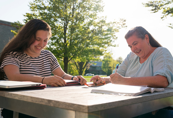 Image of adult students completing coursework outside at a table.