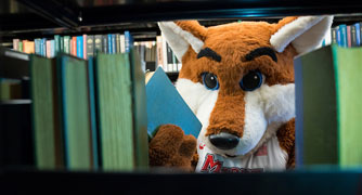 Image of Frankie the fox looking between a book shelf in the library.