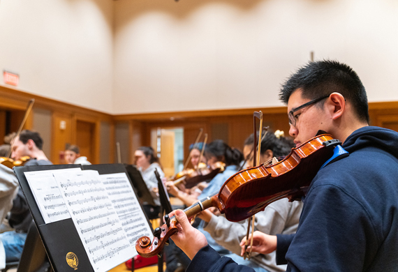 Image of student participating in orchestra rehearsal.