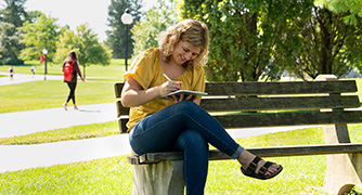 An image of student writing on a bench on campus