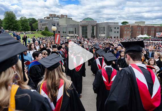 Image students wearing caps and gowns lined up on the Campus Green prior to the undergraduate commencement ceremony -  with 