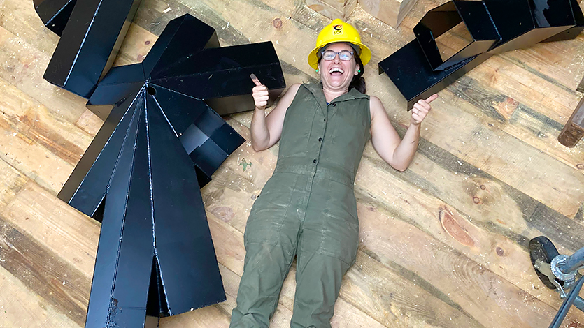 Image of Heidi Richards giving a smile and two thumbs up as she works on the treehouse’s construction. 