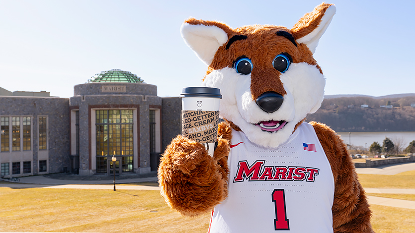 Image of Marist mascot Frankie the Fox holding a Saxbys coffee cup in front of the campus green and rotunda.