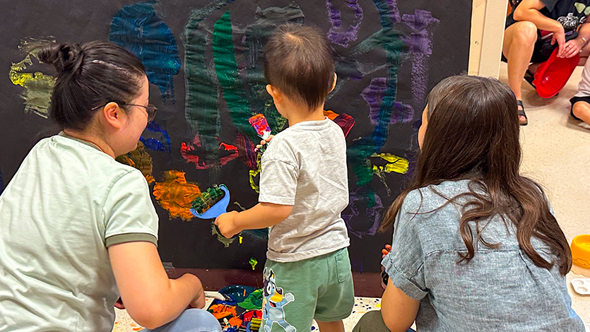 Image of Tori Hegenauer '27 (right) helps a young patron and his mom navigate a sensory activity. Photo by John Torres.&nbsp;