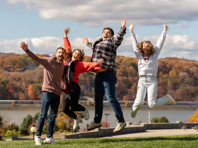 Image of a group of Marist University alumni jumping on the campus green at homecoming and reunion weekend.